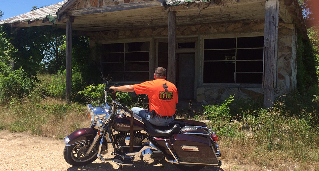 Man on a motorcycle parked outside an abandoned house